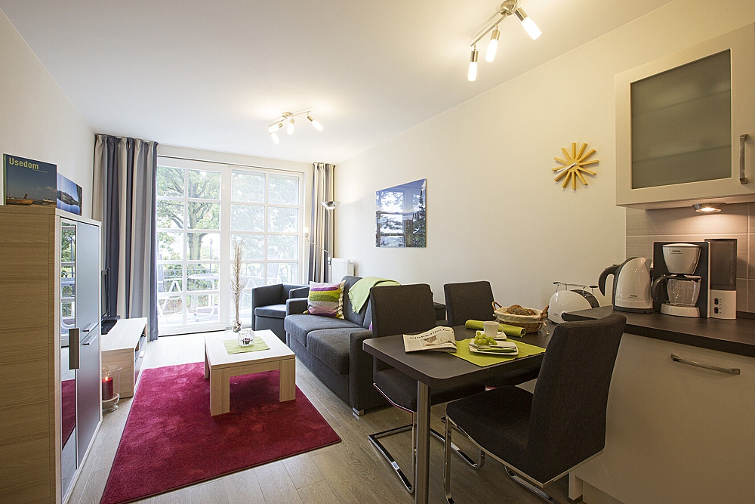 A modern living room with a sofa, a dining table, and a kitchen area with a coffee machine.