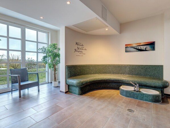 Un salon moderne avec un canapé vert aux lignes courbes, une petite table ronde et une plante en pot.