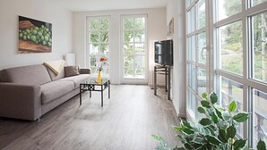A living room with a sofa, coffee table, TV, and large windows. - Residenz am Balmer See, apartment 20 with sauna, lake view and WLAN (Balm)