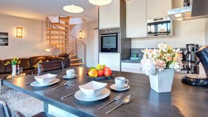 A modern kitchen with a built-in oven, a dining area with a wooden table set for two, and a spiral staircase leading to an upper level. - Residenz am Balmer See, apartment 67 with sauna, lake view and WLAN (Balm)