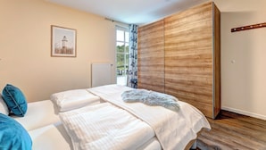 Un dormitorio con cama, armario, radiador, ventana con cortina y un cuadro en la pared.