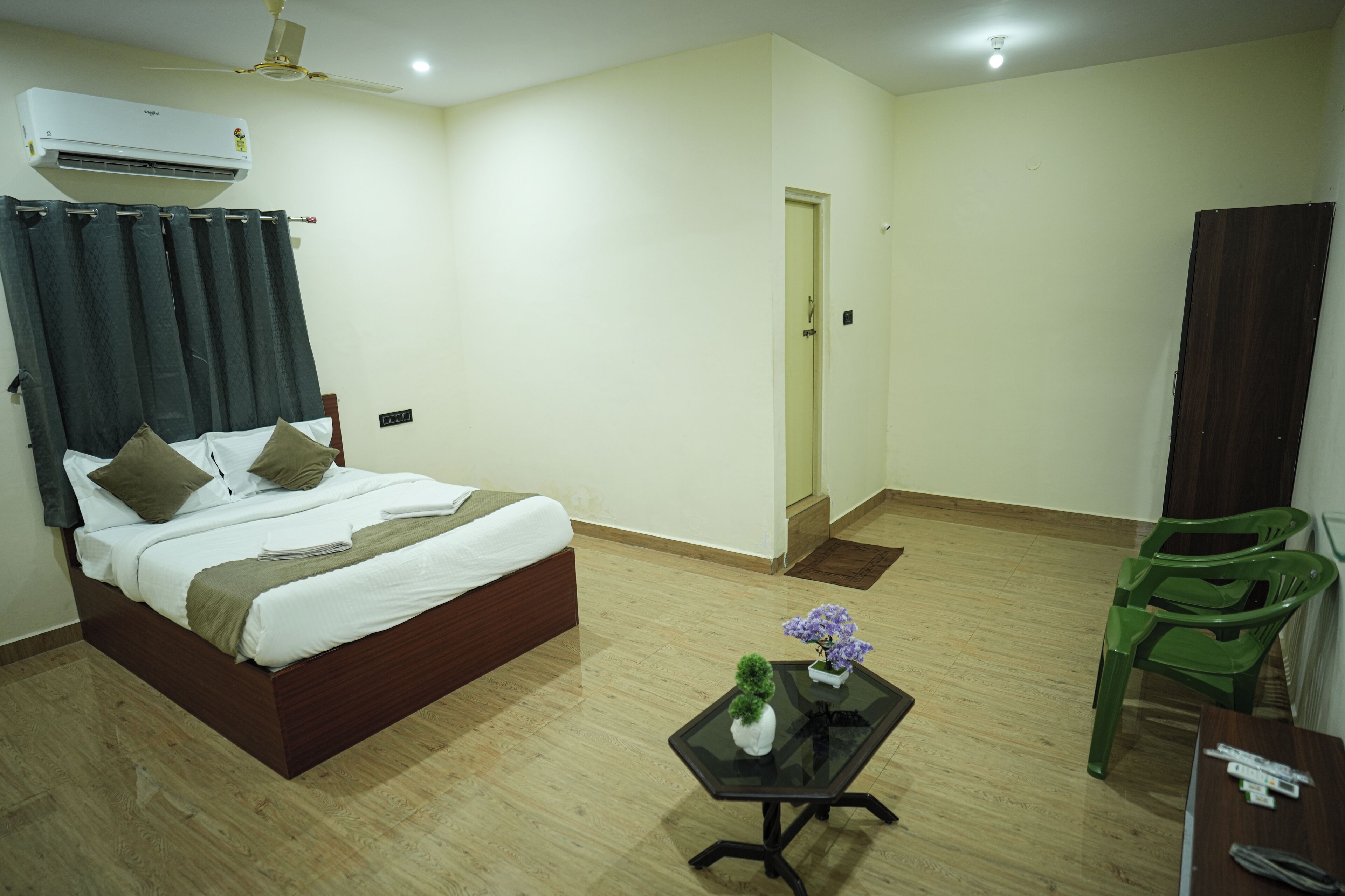 Una habitación de hotel con una cama, una pequeña mesa con un jarrón, una silla verde y un equipo de aire acondicionado.
