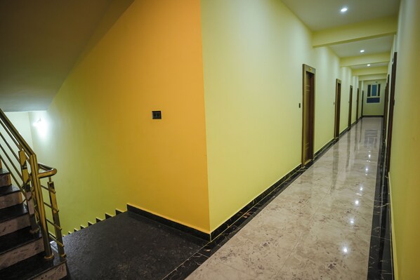 A long, narrow hallway with a marble floor and yellow walls. - Hotel Pergola (Mysore)
