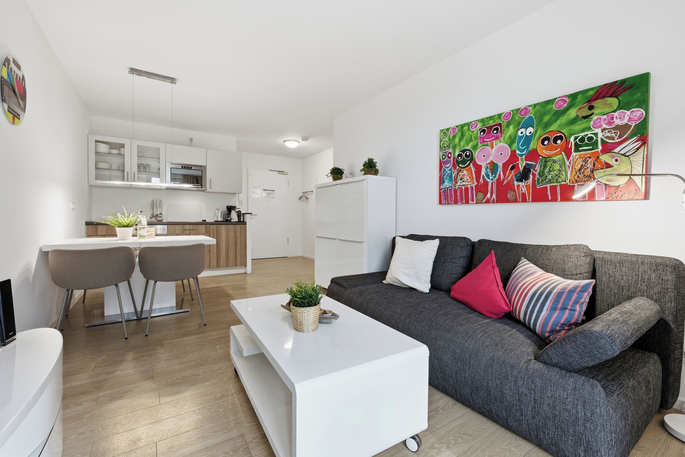 Een moderne woonkamer met een grijze bank, een witte salontafel en een kleurrijk schilderij aan de muur.
