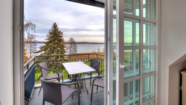 A balcony with a table and chairs, overlooking a body of water and trees.