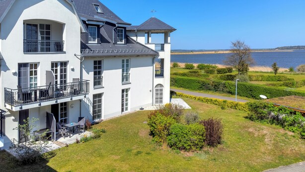 A large, two-story house with a balcony, a view of the water, and a well-maintained lawn.