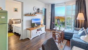 Un saló modern amb llit, televisió i zona de seients, amb una finestra gran que ofereix una vista panoràmica.