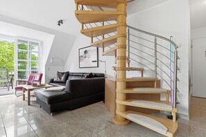 A modern living room with a wooden spiral staircase, a black leather sofa, and a large window with a view of greenery. - Residenz am Balmer See, apartment 32 - with sauna and lake view (Balm)