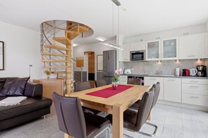 Uma cozinha moderna com armários brancos, uma mesa de jantar de madeira com cadeiras e uma escada em espiral.
