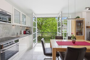 A modern kitchen with an open layout, a dining area with a table and chairs, and a view of greenery through large windows. - Residenz am Balmer See, apartment 32 - with sauna and lake view (Balm)