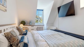 A bedroom with a bed, pillows, a desk, a chair, a TV, and a window.