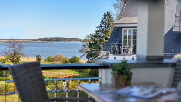 A balcony with a view of a lake, a chair, and a table with a plant.