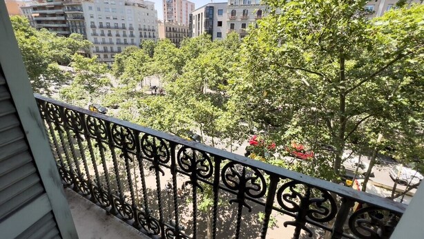 Un balcón con barandilla de hierro forjado que da a una vista panorámica de la ciudad con edificios y árboles.