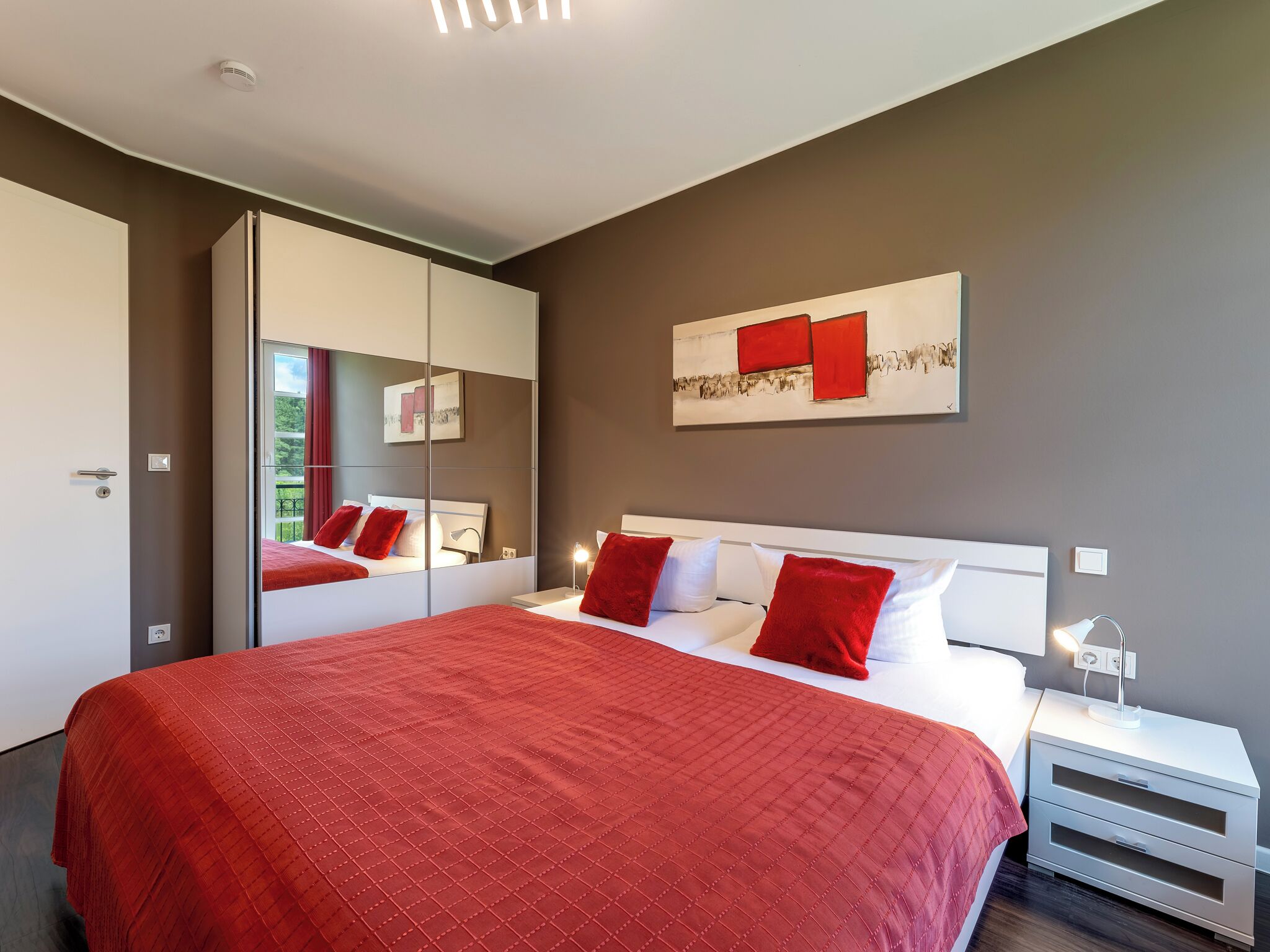 A modern bedroom with a large bed, a mirror cabinet, and a painting on the wall.