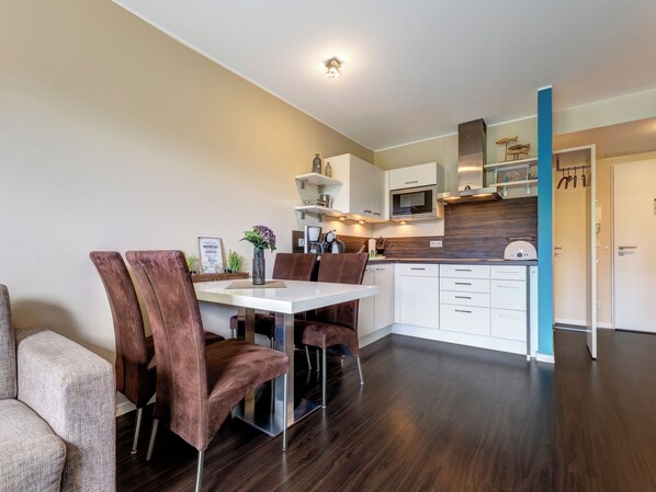 Una cocina moderna con armarios blancos, un microondas y un horno empotrado. Hay una zona de comedor con una mesa blanca y sillas marrones.
