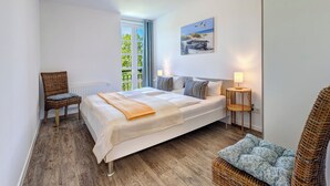 Une chambre avec un grand lit, une chaise, une petite table et une vue sur la verdure par la fenêtre.