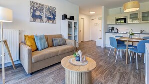 Un salon moderne avec un canapé beige, une table basse ronde en bois et un coin repas avec des chaises bleues.