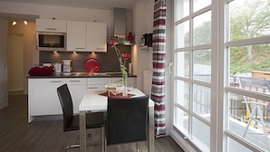 Cocina moderna con armarios blancos, un microondas y un hervidor rojo. Hay una mesa de comedor con dos sillas y un jarrón con flores rojas.