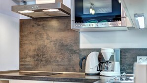 Une cuisine moderne dotée d’une hotte en acier inoxydable, d’un four encastré et d’une machine à café posée sur le plan de travail.