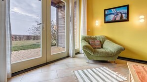 Une pièce avec un fauteuil vert, un tableau accroché au mur et une vue sur un espace extérieur, visible à travers de grandes portes vitrées.