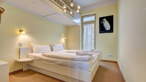 Un lit bien fait, avec du linge de lit blanc et une petite table de chevet, une fenêtre avec des rideaux et un tableau représentant un chat accroché au mur.
