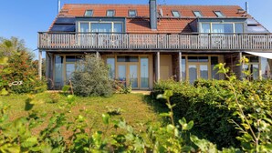 Une maison à deux étages dotée d’un balcon, de grandes fenêtres et d’un toit recouvert de tuiles rouges.