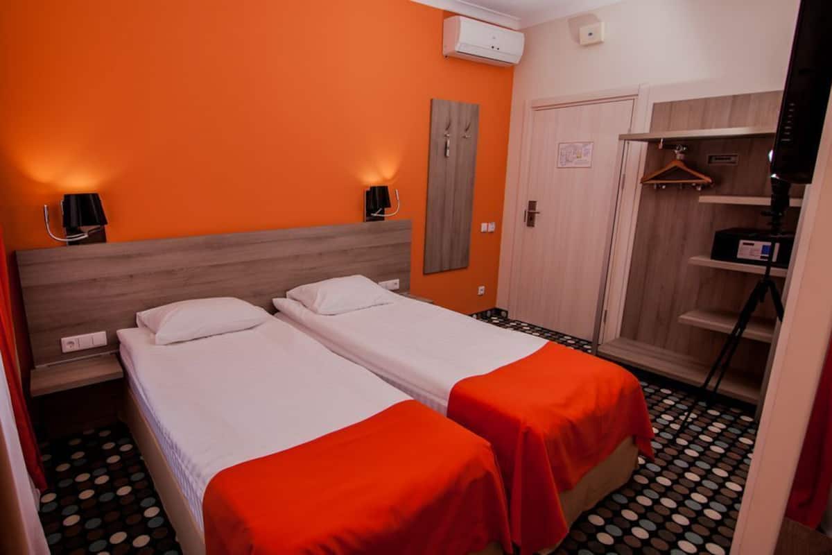 Une chambre d’hôtel avec deux lits, un mur orange, une armoire et un miroir.