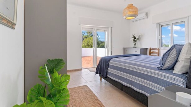 Een slaapkamer met een bed, een nachtkastje, een kamerplant en uitzicht op de omgeving.