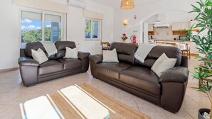 Een moderne woonkamer met twee bruine leren banken, een houten salontafel en een groot raam met luxaflex.