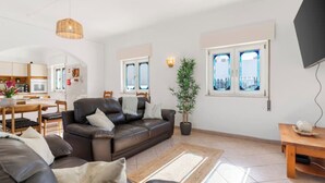 Een moderne woonkamer met een bruine leren bank, een eettafel met stoelen, een potplant en uitzicht op zee door grote ramen.