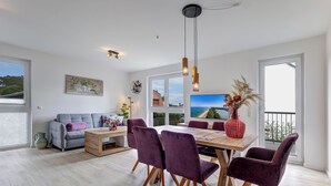 A modern living room with a sofa, coffee table, and dining area with chairs. There is a large window with a view of the outdoors. - Bernsteinquartier, apartment 05.49 "Ferienglück" in Kölpinsee - close to the beach & stylish (Kölpinsee)
