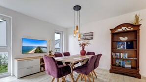A modern dining area with a wooden table, purple chairs, a TV on the wall, and a bookshelf with books. - Bernsteinquartier, apartment 05.49 "Ferienglück" in Kölpinsee - close to the beach & stylish (Kölpinsee)