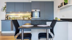 Una cocina moderna con armarios grises, horno integrado y una zona de comedor con dos sillas negras y una mesa redonda.