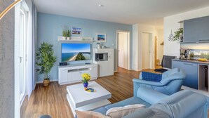 Una sala moderna con un televisor de pantalla plana grande, un sofá, una mesa de centro y una zona de cocina con armarios y una encimera.