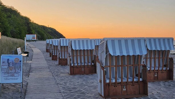 Cabañas de playa con toldos a rayas, un camino de madera y un cartel.