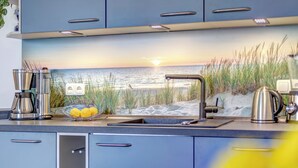 Cocina moderna con salpicadero empotrado que representa una escena de playa, electrodomésticos de acero inoxidable y un lavamanos con grifo.