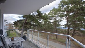 Un balcón con mesa y sillas, con vista a un sendero y árboles.