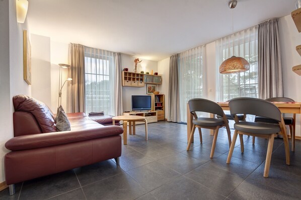Una sala de estar moderna con sofá, sillones, televisor y comedor.