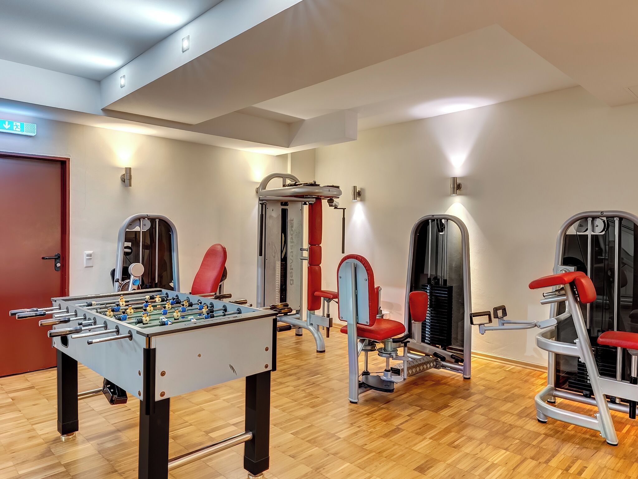 A gym with a foosball table, red exercise chairs, and various workout machines.