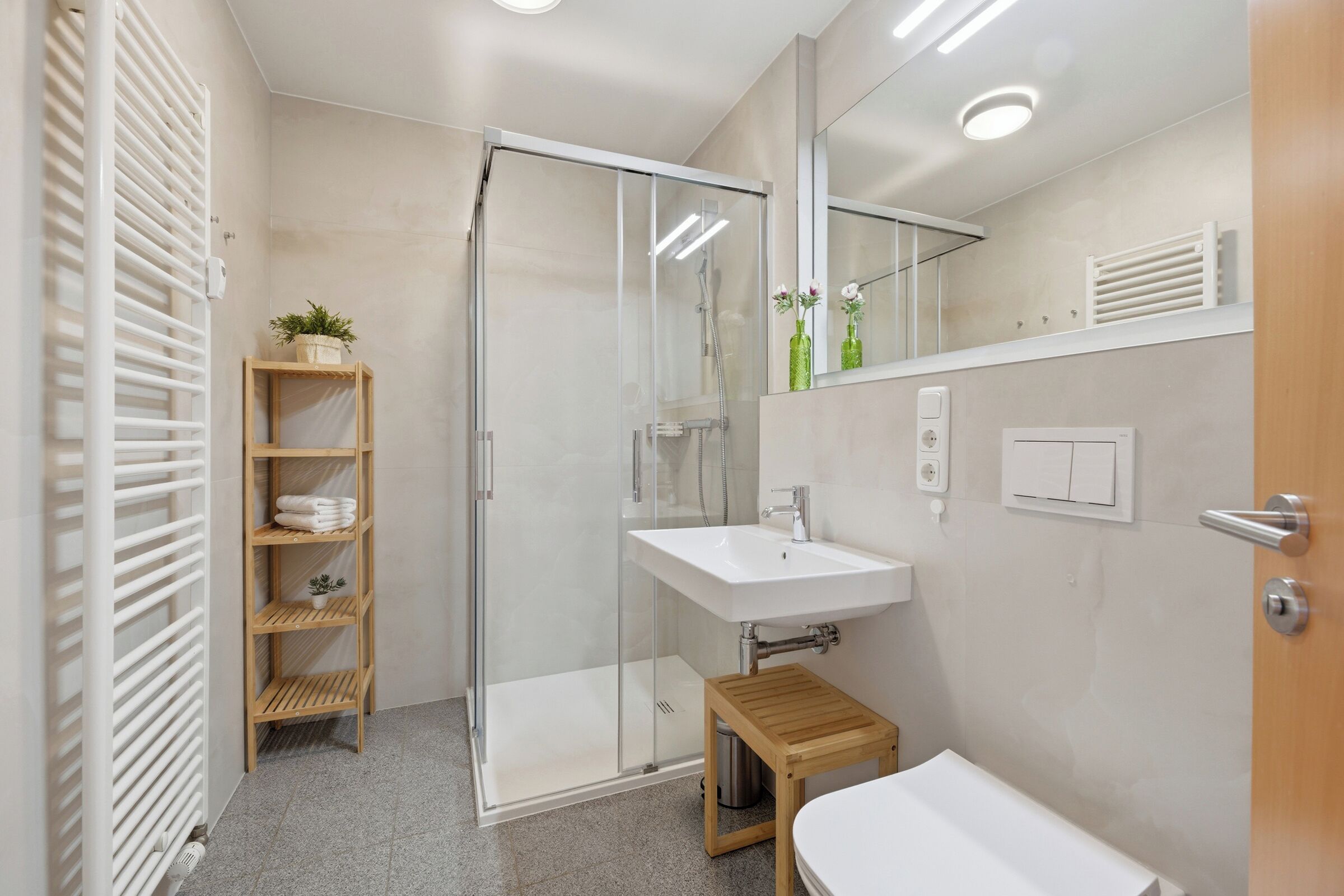 Un bagno moderno con box doccia in vetro, un lavandino bianco e una mensola in legno con asciugamani.