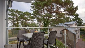 Un balcón con sillas de mimbre y una mesa, con vista a un jardín y una casa.