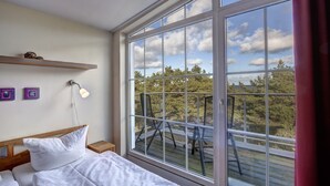 A bedroom with a large window, a bed, a bedside table, and a wall-mounted shelf. - Ostseeresidenz Gorki Park, Whg. 18:20 m to the sandy beach, 5 star comfort (Heringsdorf)