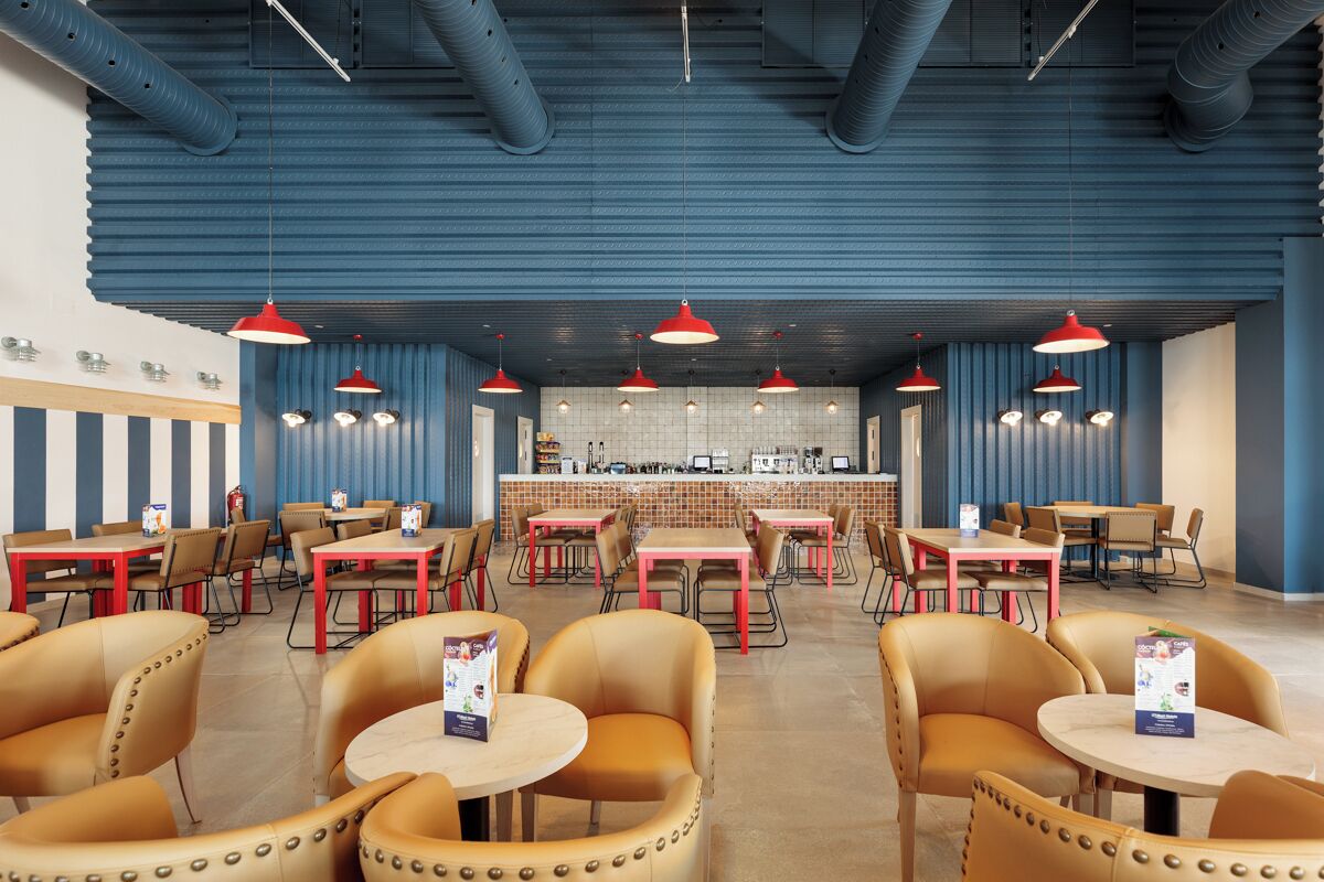 A restaurant with multiple tables and chairs, a bar area, and hanging red pendant lights.