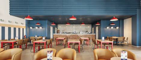 A restaurant with multiple tables and chairs, a bar area, and hanging red pendant lights.