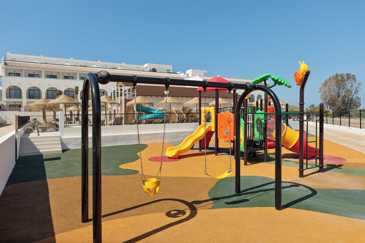 A playground with swings and slides, a building with arched windows, and a clear sky.