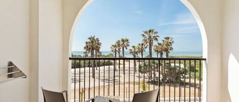 A balcony with a view of the beach, palm trees, and a clear sky.