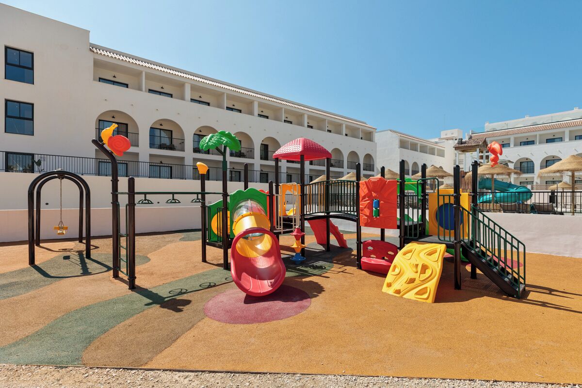 A playground with slides and climbing structures, surrounded by a building with arched windows and balconies.