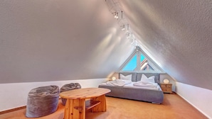 A cozy attic bedroom with a sloped ceiling, a bed, a small table, and bean bags.