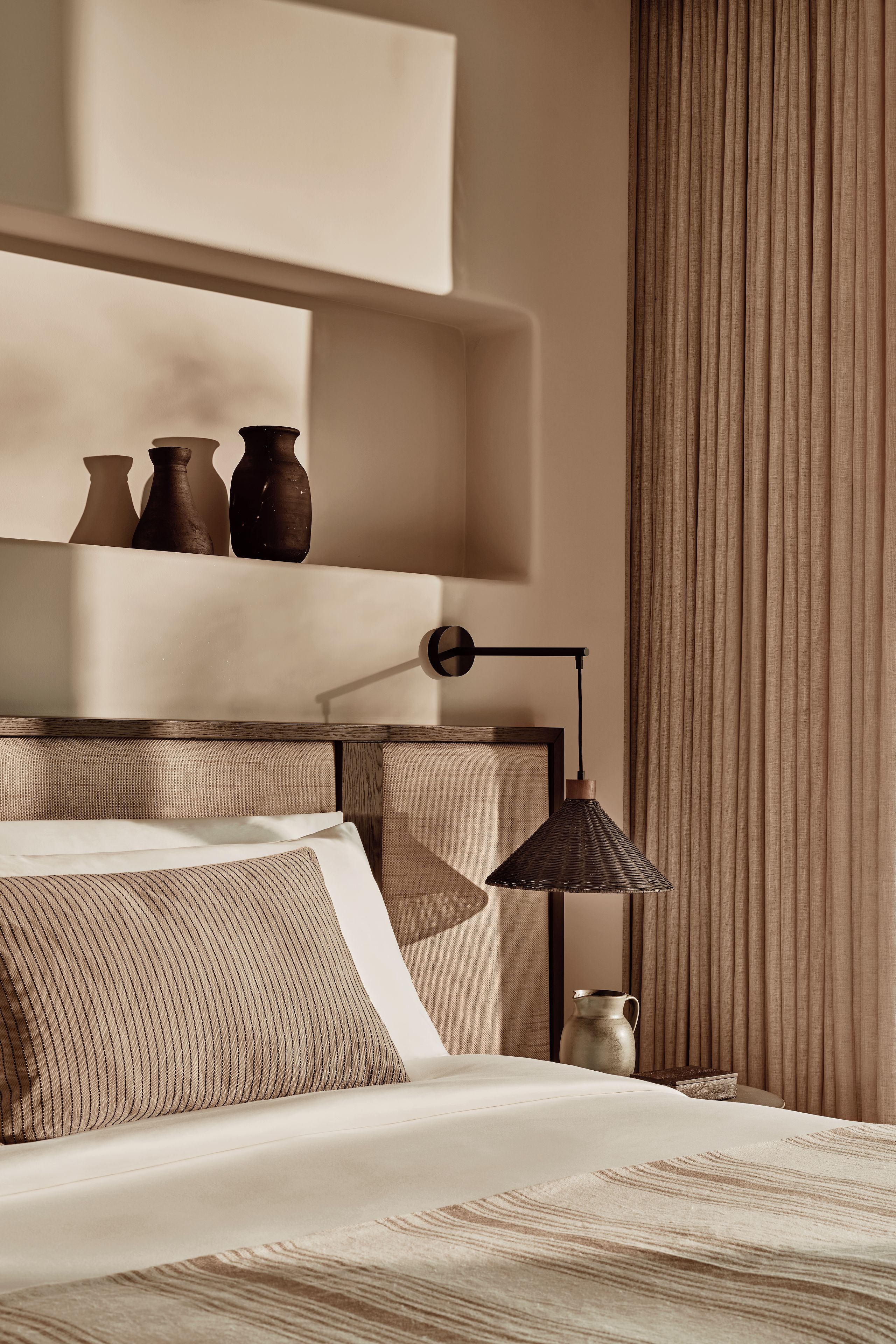 A modern bedroom with a bed, bedside table, lamp, and decorative vases.