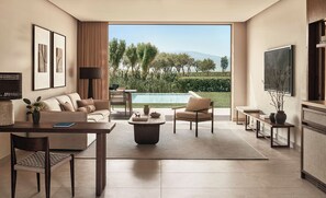 A modern living room with a sofa, armchairs, a coffee table, and a TV. There is a pool visible through the glass doors. - Ikos Kissamos - All Inclusive (Kissamos)
